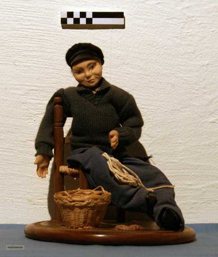 Zittende vissersfiguur met vissersmand en touw gemonteerd op rond houten paneel